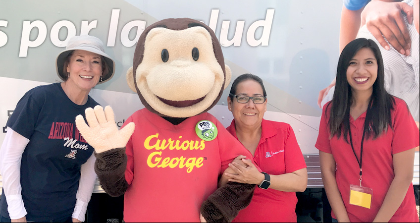 Tucson Mobile Health Unit at the 2019 Tucson Festival of Books on the UA Mall. Left to right: Debbie C. Tomayo, Curious George, Andrea Contreras, and Sheila Soto.
